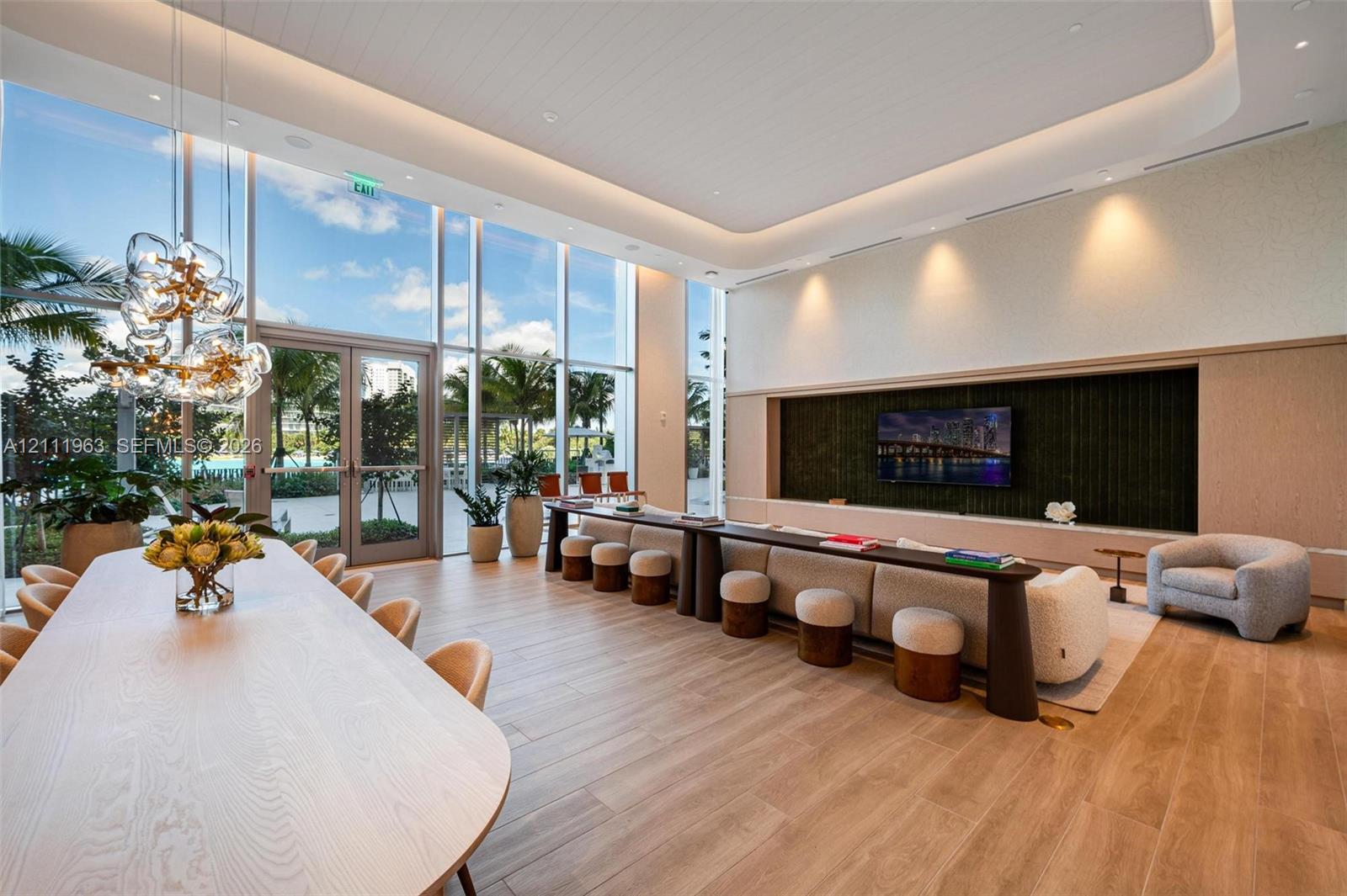 High-ceiling living area featuring recessed cove lighting, wood-finish flooring, custom built-in cabinetry with integrated media wall, and a multi-globe pendant light fixture