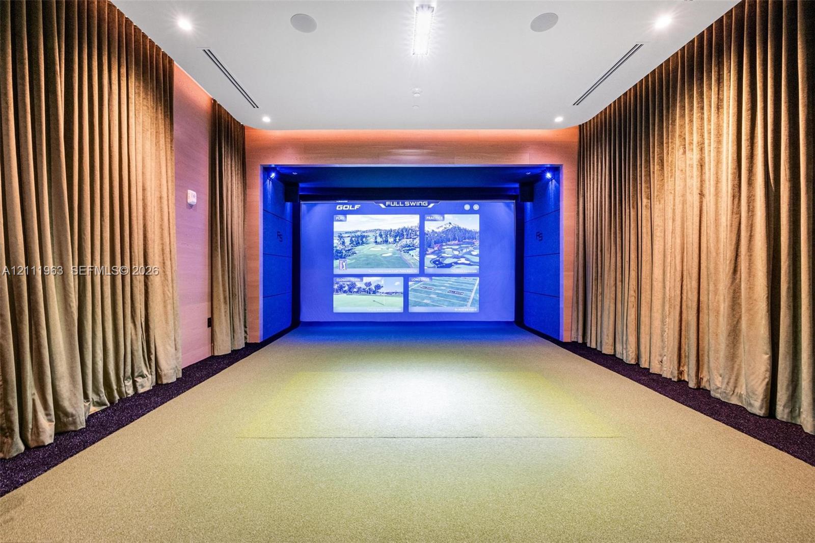 Media room featuring wood-paneled walls, recessed ceiling lighting, a built-in projection system, and a designated synthetic turf simulation area