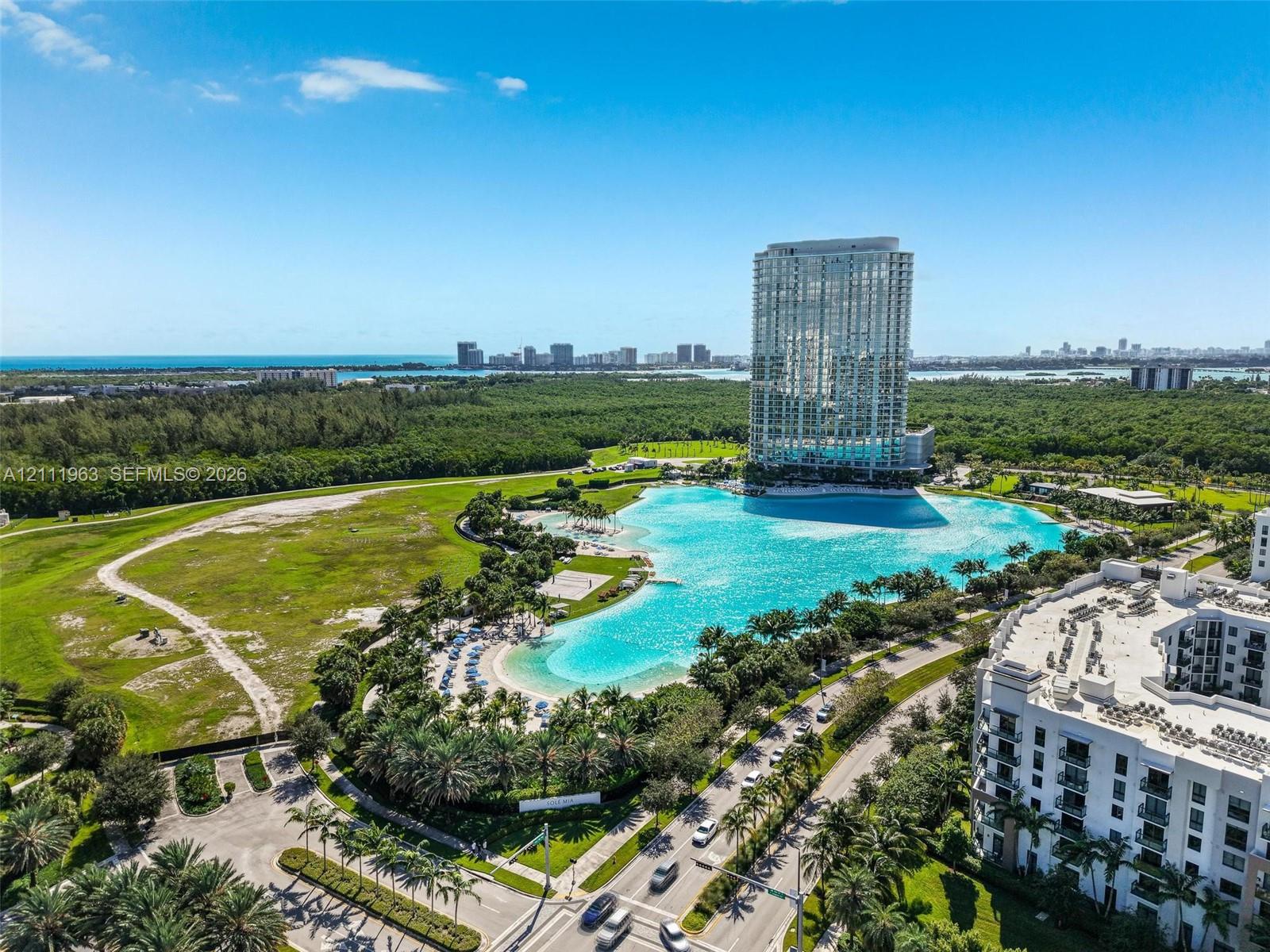 Aerial perspective featuring a large crystalline lagoon, coastal skyline, and dense woodland surroundings