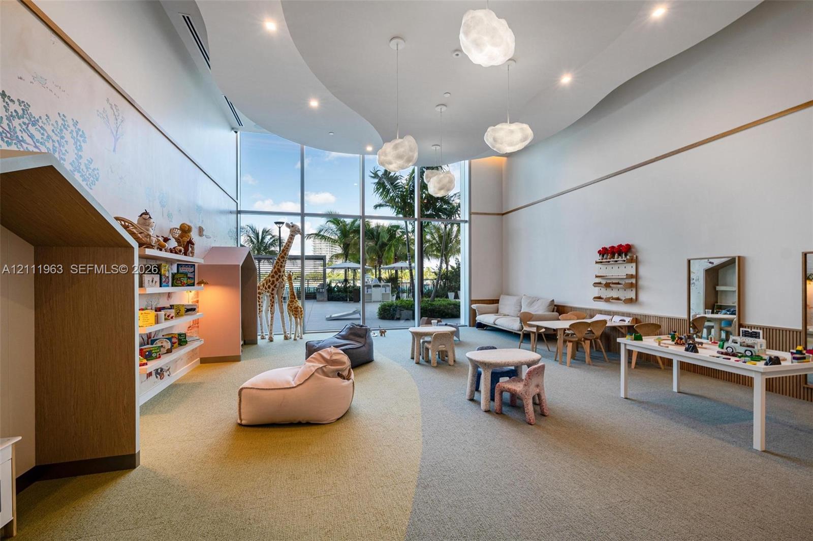 Expansive room featuring floor-to-ceiling glass windows, recessed ceiling architecture with cloud-shaped pendant lighting, and custom wall-mounted shelving with built-in reading nooks