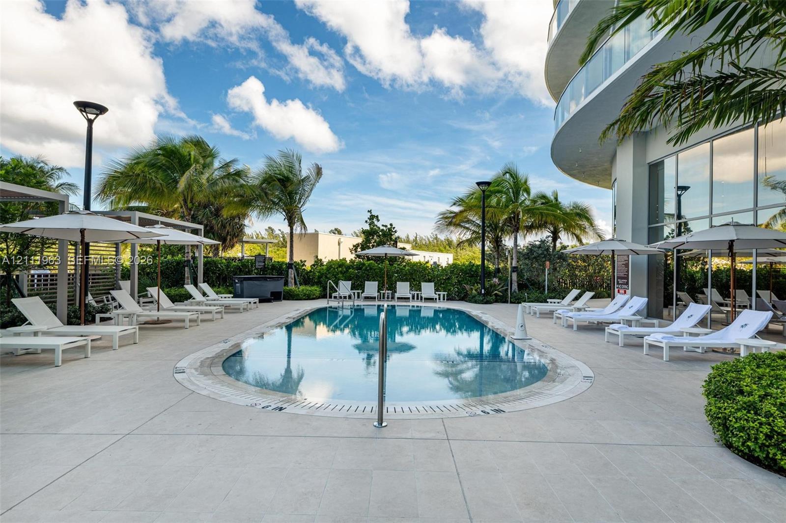 Outdoor grilling area featuring a stainless steel built-in barbecue station under a louvered metal pergola, large-format tile patio, and swimming pool