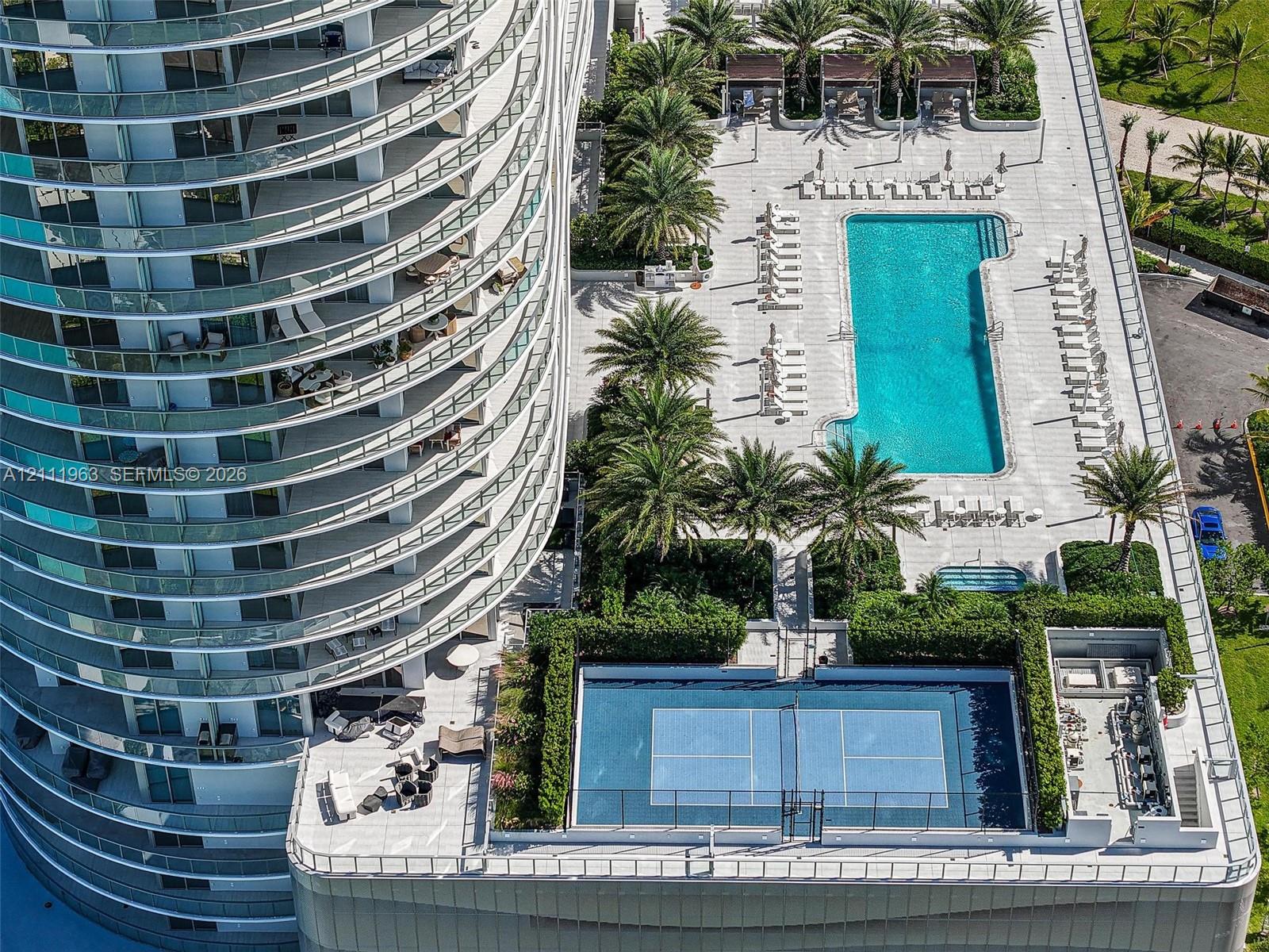 Elevated recreational deck featuring a swimming pool, tennis court, and lush landscaping