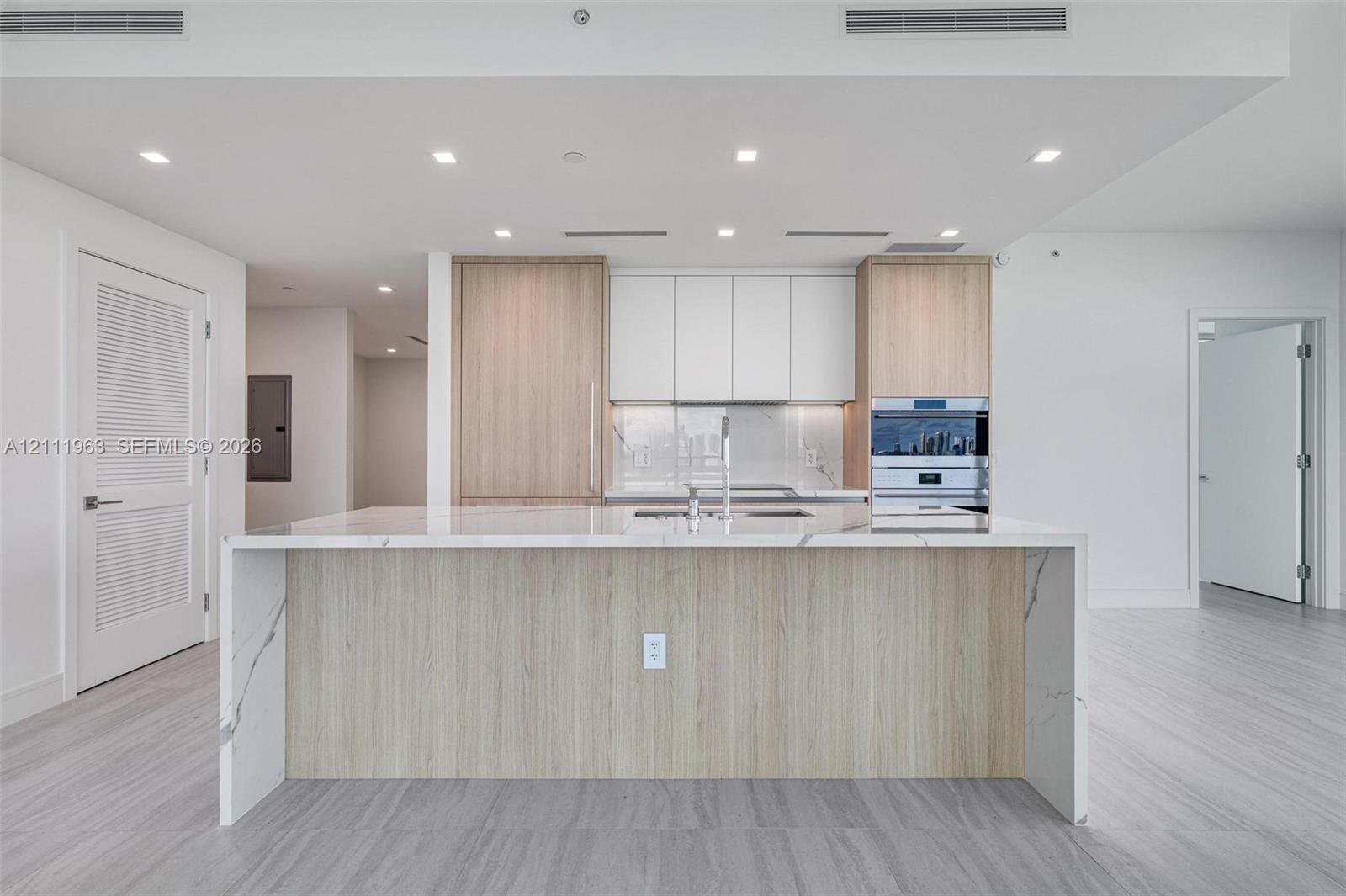 Floor-to-ceiling glass walls, expansive wraparound terrace with metal railings, kitchen island featuring waterfall-edge stone countertop, wood-finish cabinetry, and large-format tile flooring