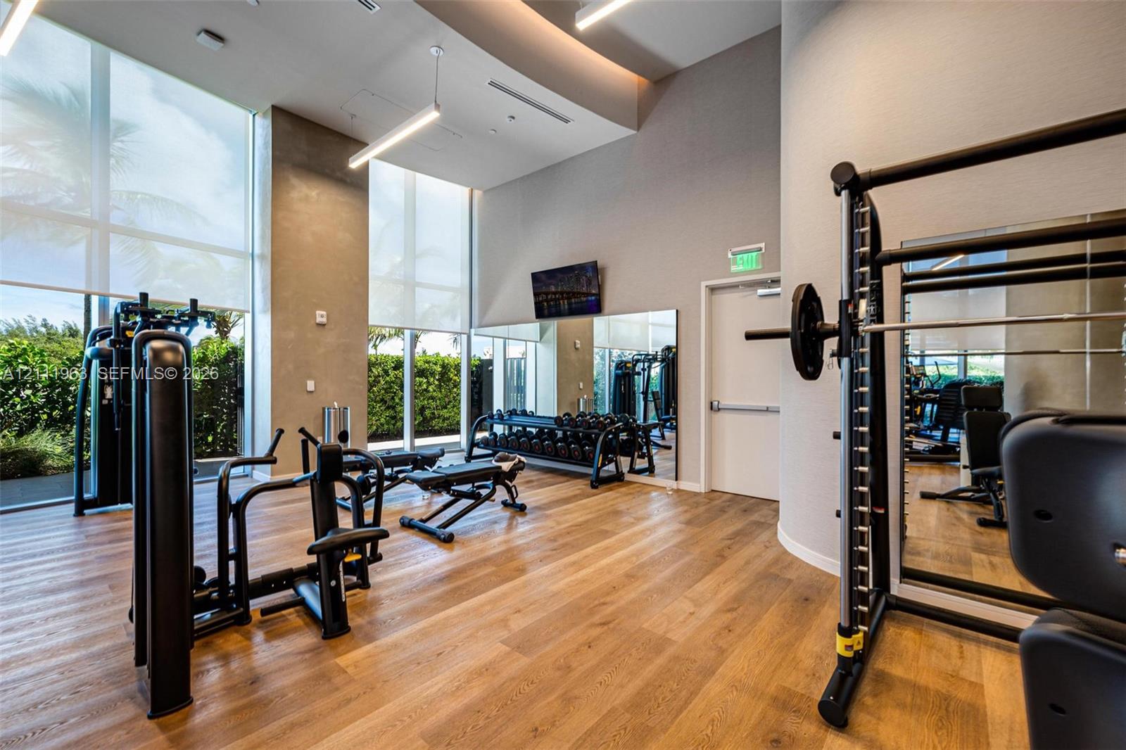 Fitness center featuring wood-finish flooring, floor-to-ceiling windows with roller shades, linear pendant lighting, and wall-to-wall mirrors