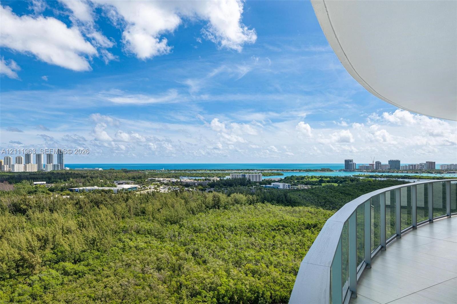 Elevated balcony featuring glass railings and panoramic landscape scenery including a man-made lagoon and coastal horizon