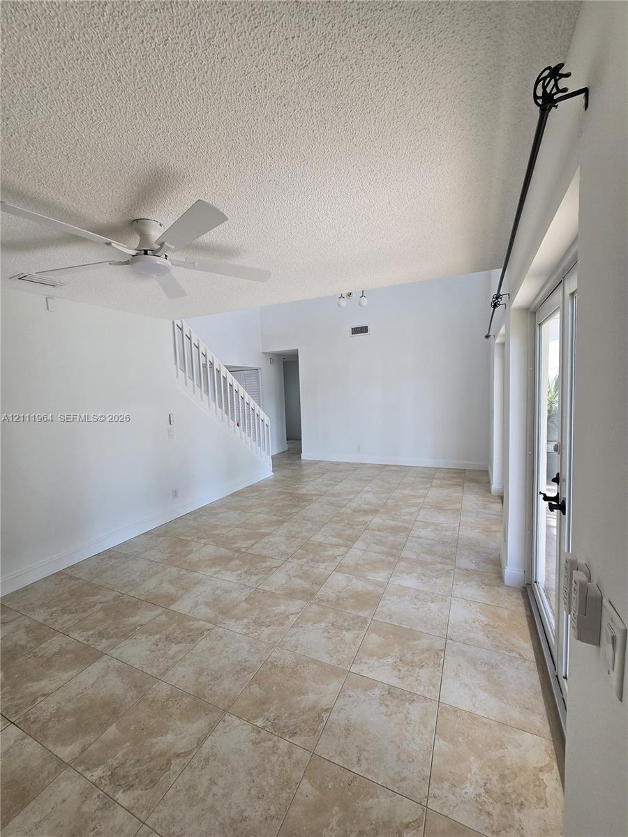 Open living area featuring vaulted ceilings, neutral tile flooring, a white staircase with wooden balusters, a ceiling fan, and double glass-panel doors