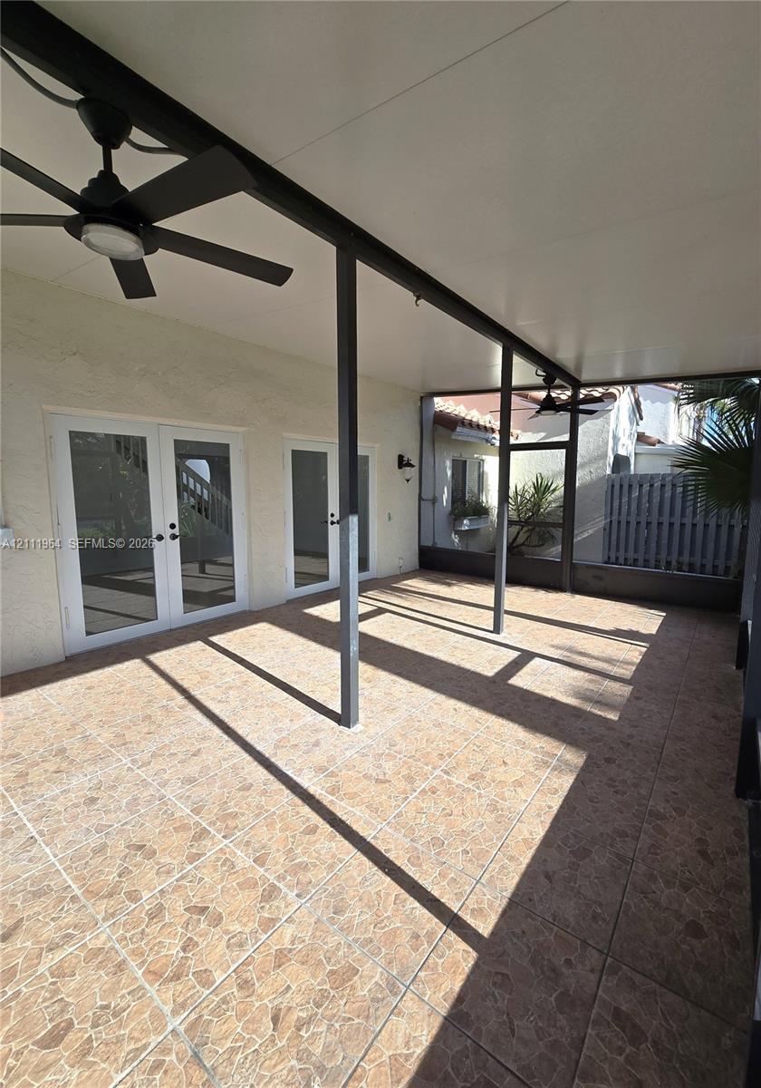Covered patio featuring stone-tile flooring, dual ceiling fans, and screened-in enclosure with double French doors
