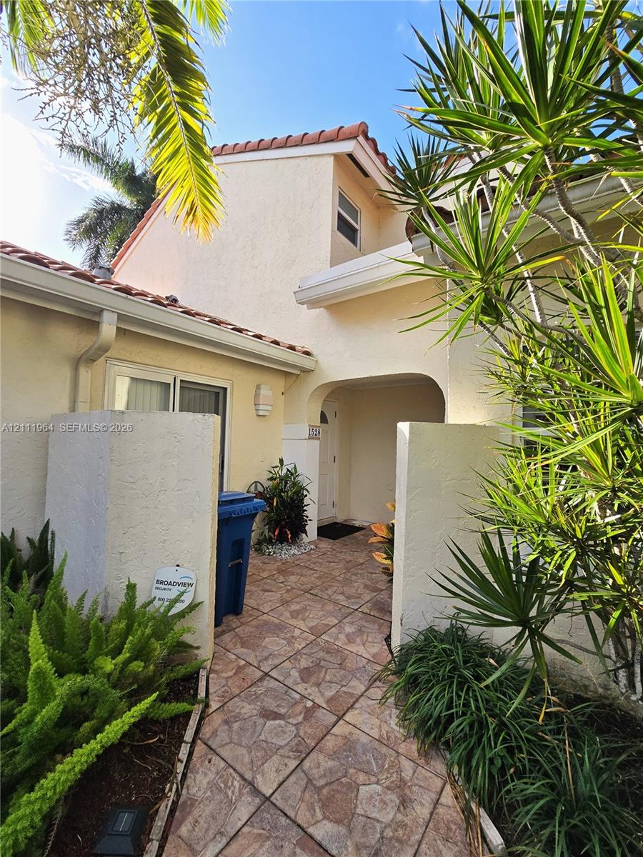 Stucco exterior with a multi-level roofline, clay tile accents, and a stone-paver walkway leading to a covered entryway