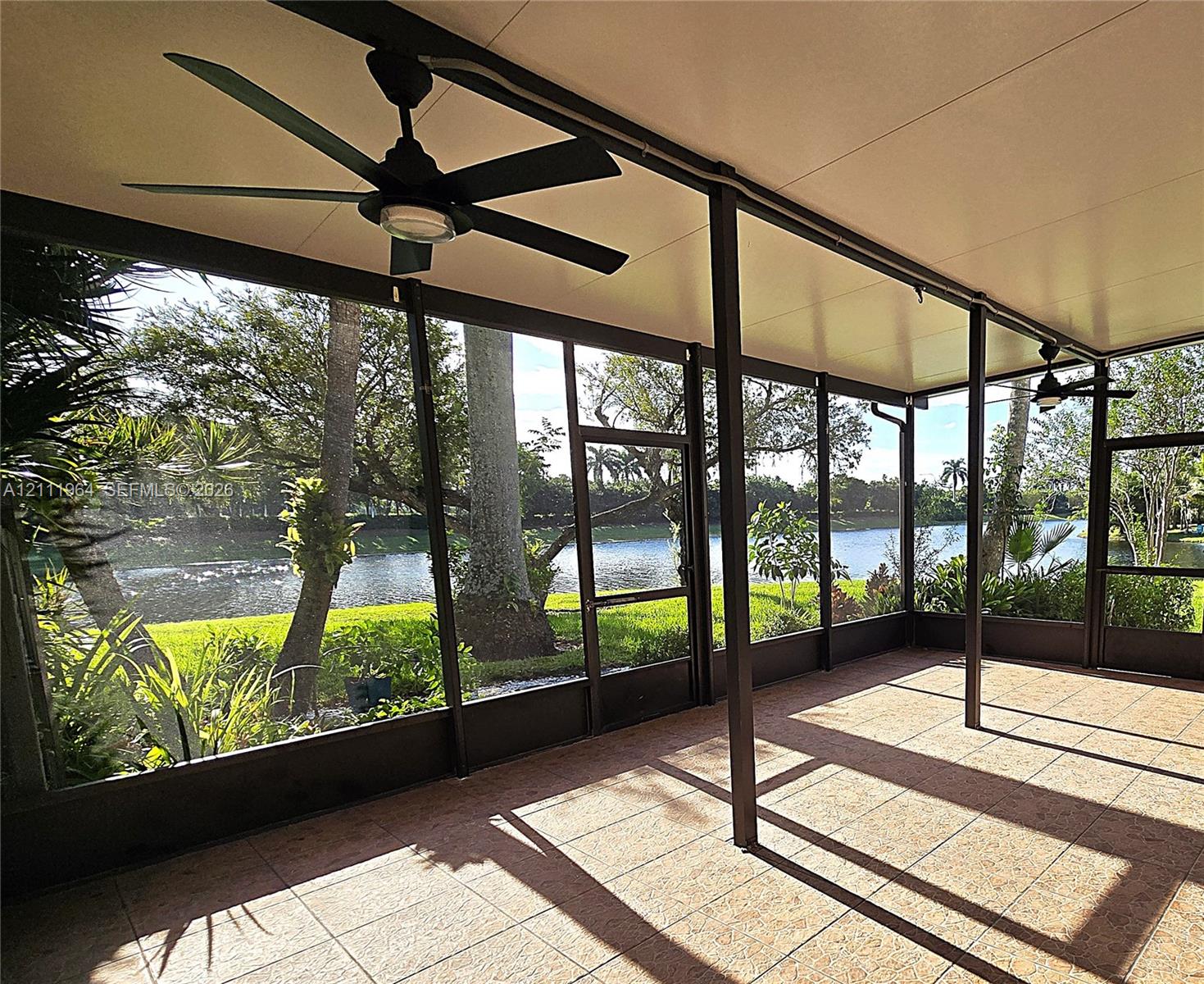 Screen-enclosed patio featuring a solid roof, large format tile flooring, and matte black ceiling fans, overlooking a waterfront setting Screen-enclosed patio featuring a solid roof, large format tile flooring, and matte black ceiling fans, overlooking a waterfront setting