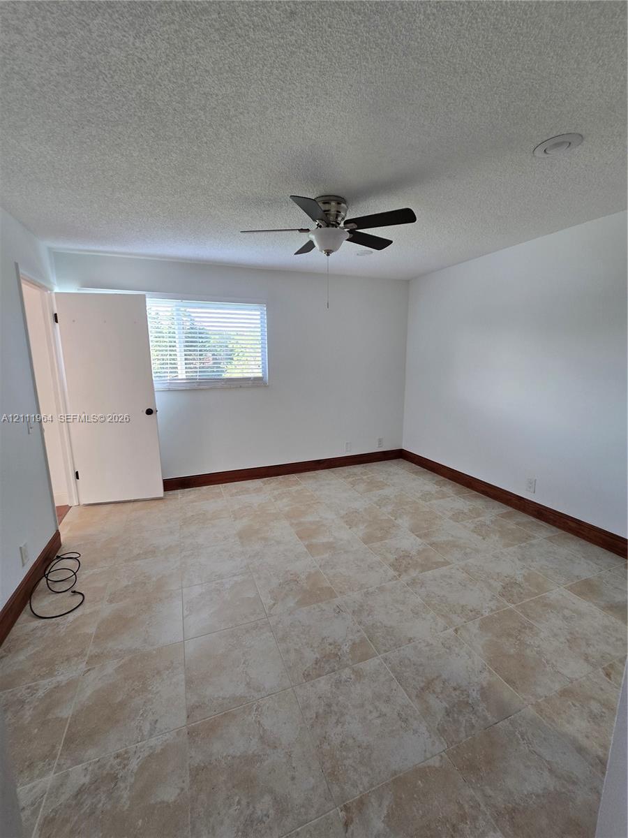 Neutral-toned tile flooring, dark wood-finished trim, ceiling-mounted fan, and horizontal window blinds