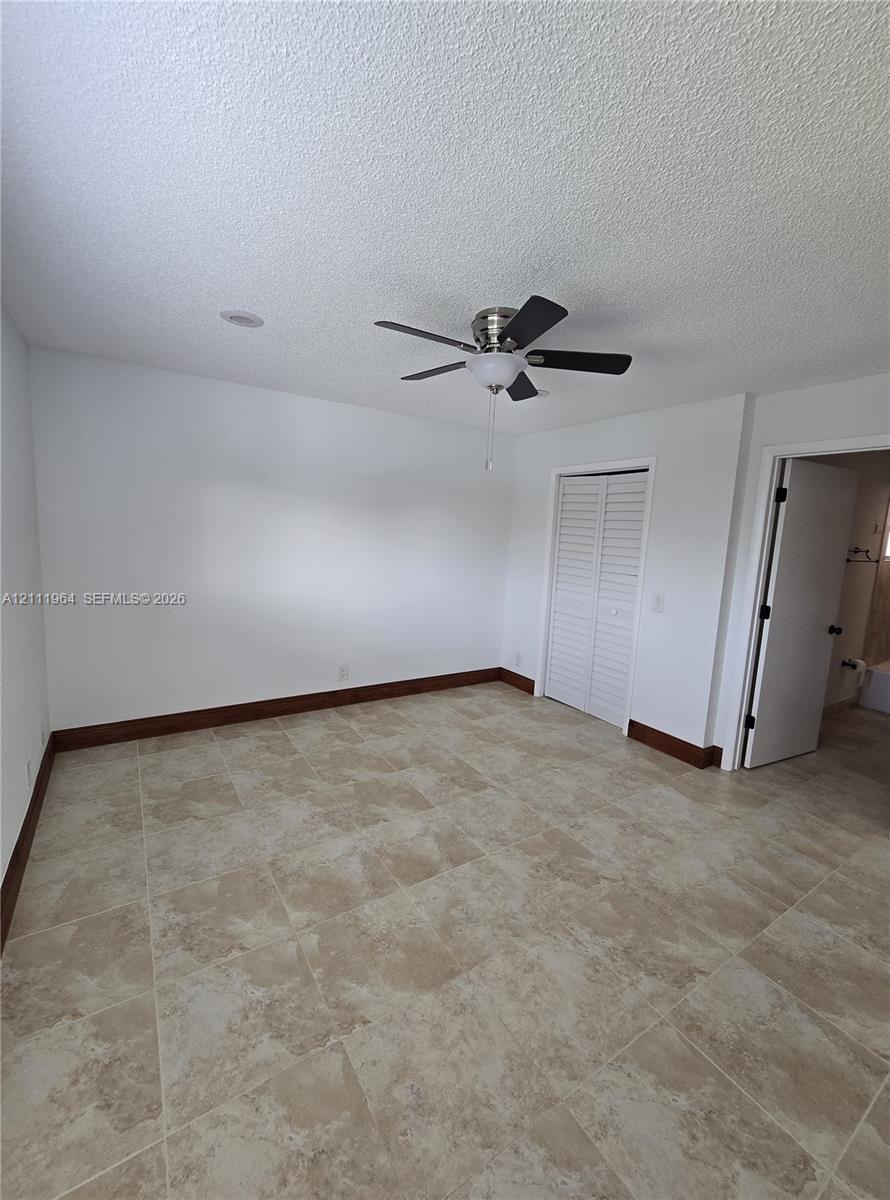 Neutral-toned tile flooring, ceiling fan with integrated lighting, and louvered-style closet doors