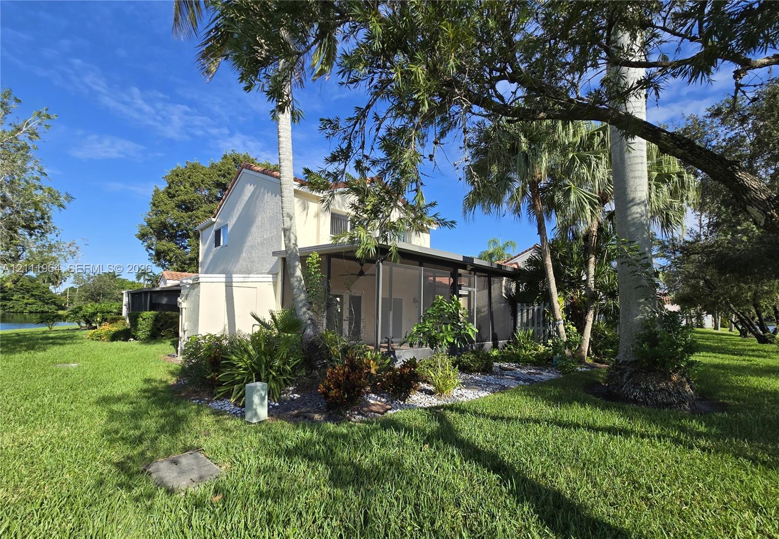 Two-story exterior featuring a stucco facade, tile roof, screened-in porch, mature palm trees, and expansive lawn