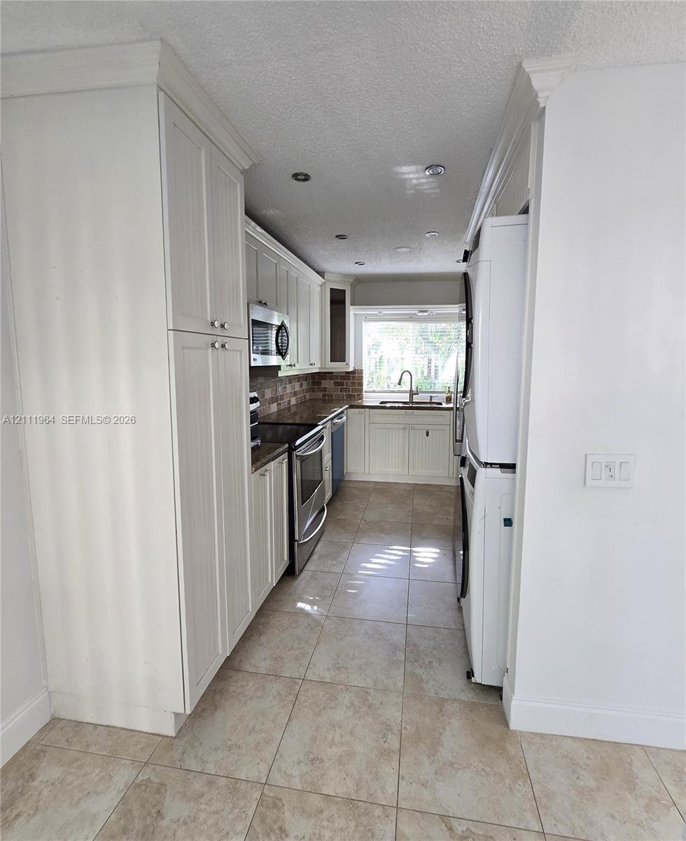 Kitchen featuring white shaker-style cabinetry, stainless steel appliances, tiled backsplash, stone-finish floor tile, and recessed lighting