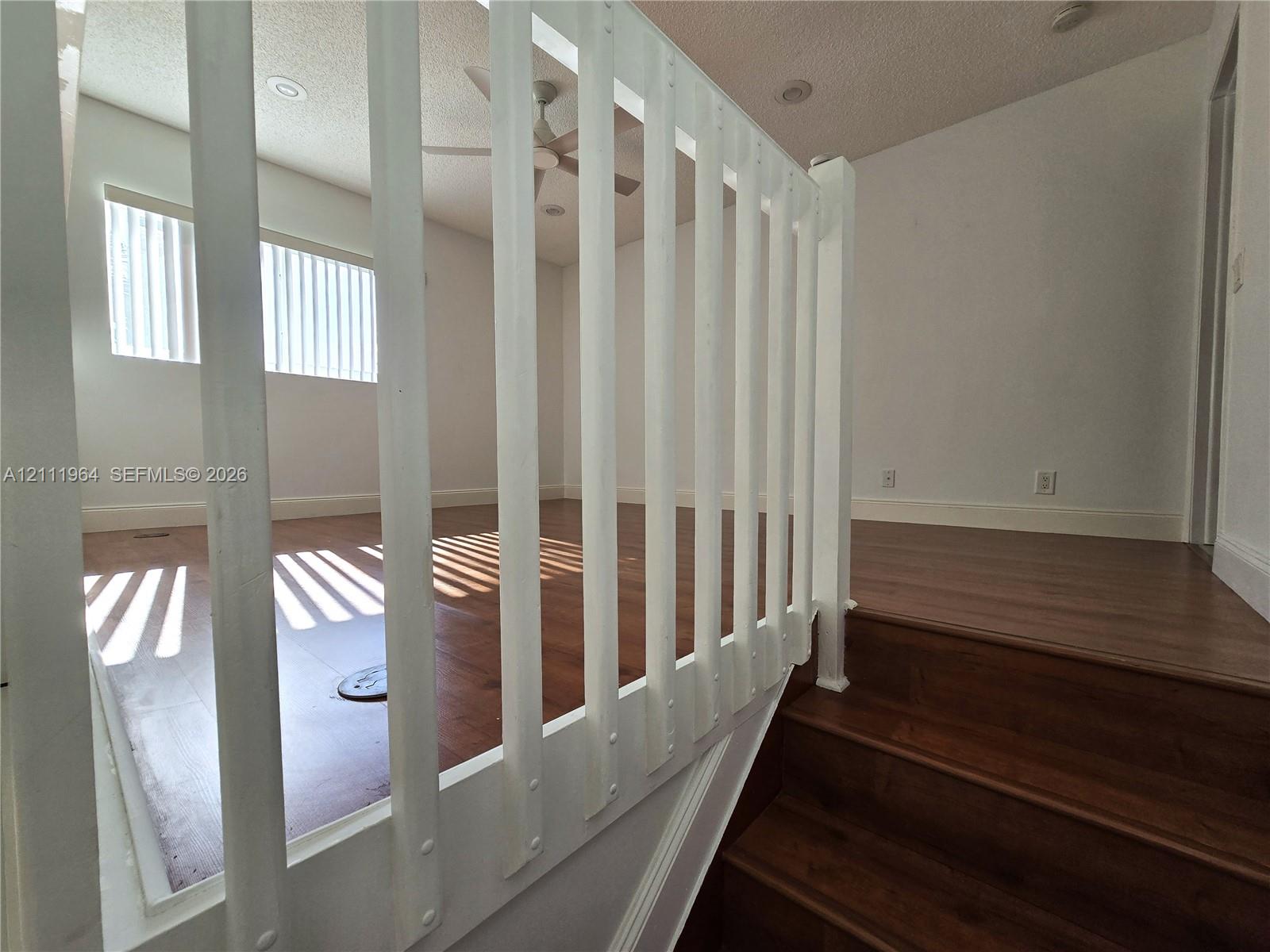 Wood-finish flooring, white vertical baluster railing, recessed ceiling lighting, and a ceiling fan