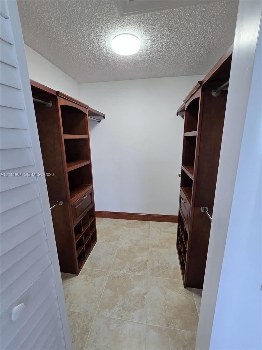 Walk-in closet featuring custom wood-finish built-in cabinetry, integrated shelving, shoe cubbies, and tile flooring