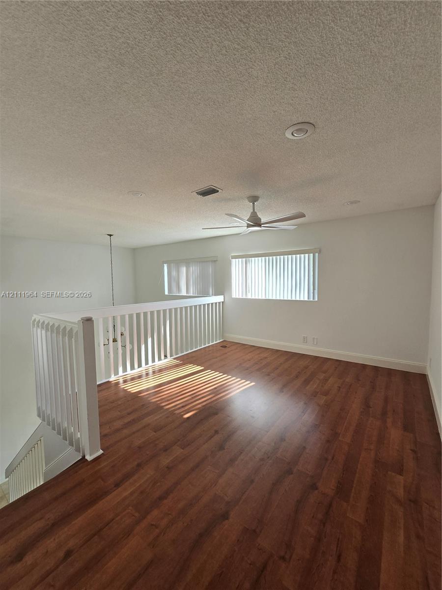 Open floor plan featuring wood-finish flooring, white spindle railing, ceiling fan, and recessed lighting