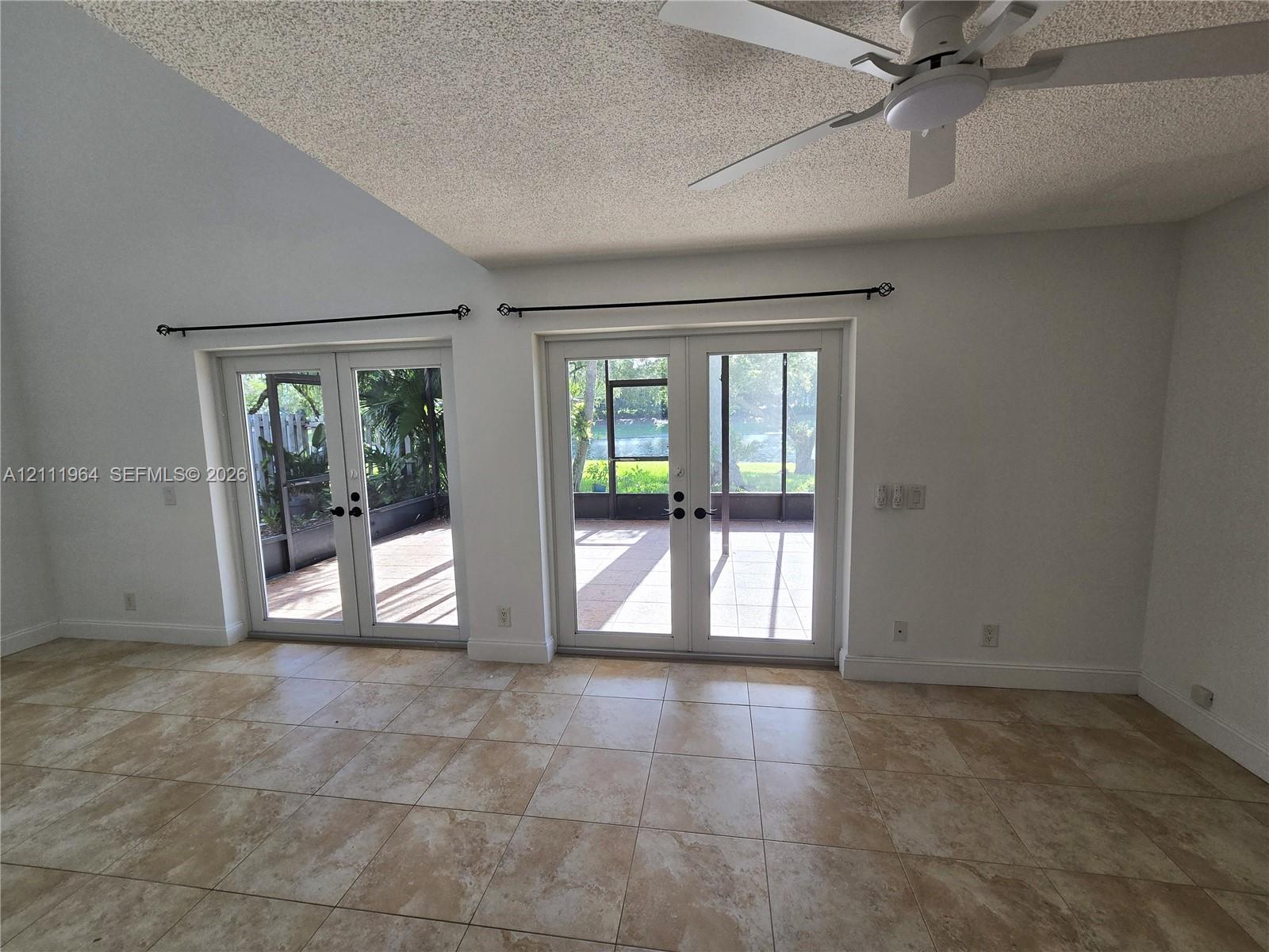 Vaulted ceilings featuring a white finish, neutral-toned tile flooring, dual sets of glass-paned double doors, and a ceiling-mounted light fixture with a fan