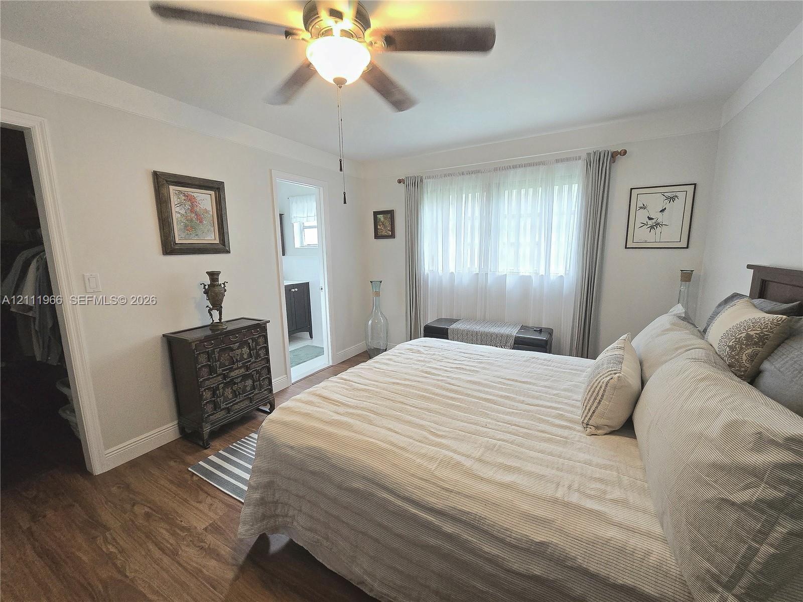 Room featuring wood-finish flooring, a ceiling fan with integrated light fixture, crown molding, and a walk-in closet