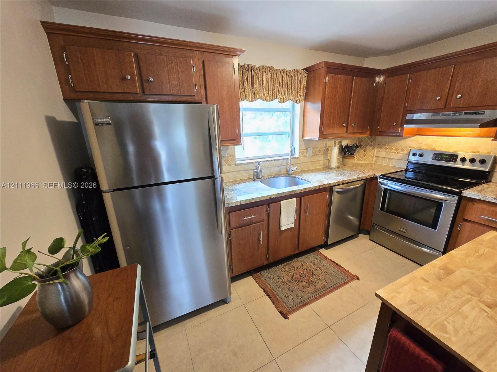Kitchen featuring wood cabinetry, stainless steel appliances, tile flooring, and a single-basin sink