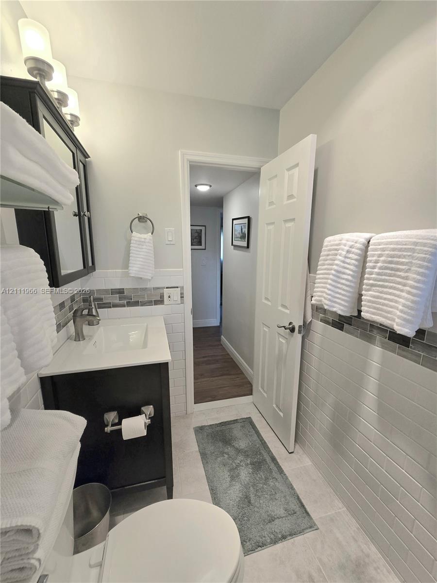 Bathroom featuring a dark wood-finish vanity with a white rectangular sink, white subway tile walls with horizontal glass tile accents, and a six-panel door