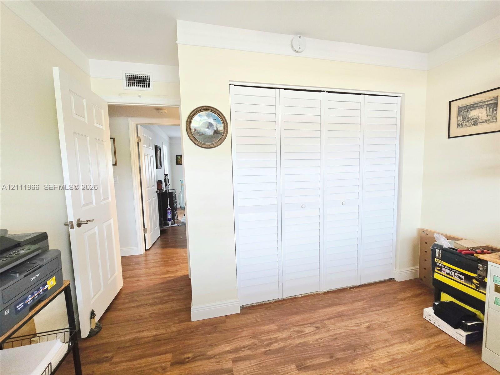 Interior room featuring wood-finish flooring, white louvered closet doors, and a six-panel interior door