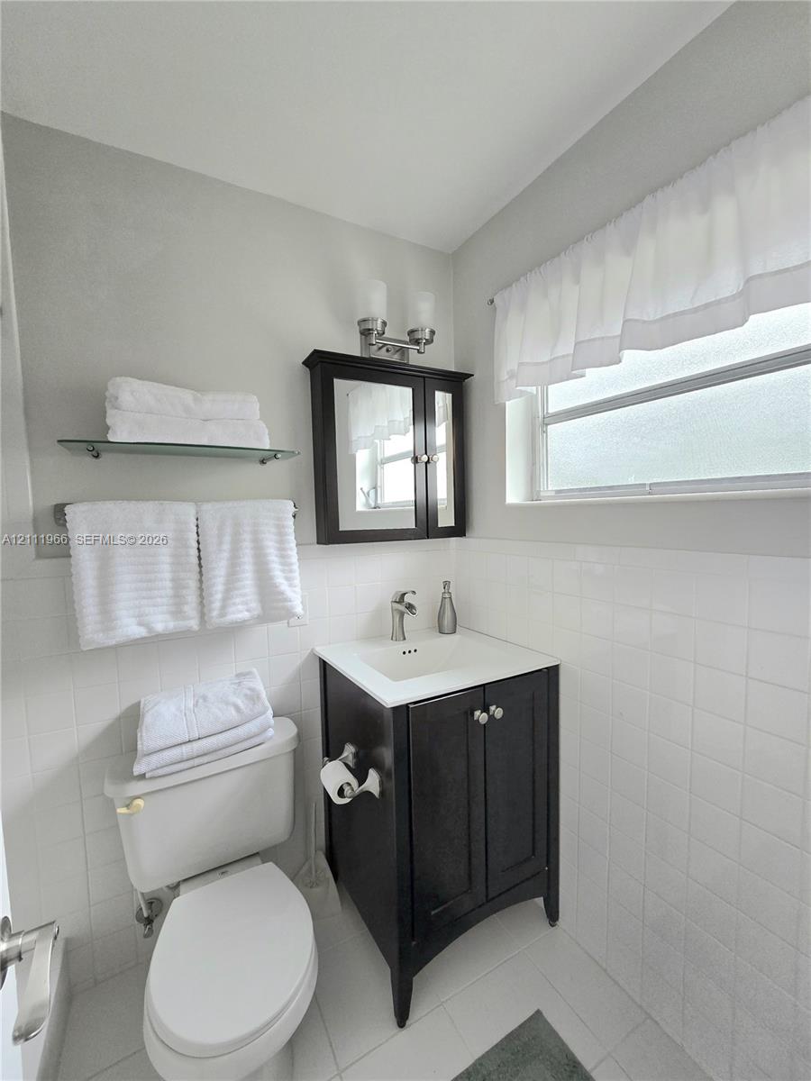 Dark-finish wooden vanity with a white countertop and integrated sink, complemented by a matching mirrored medicine cabinet, a wall-mounted glass shelf, and classic white tiled wall surfaces