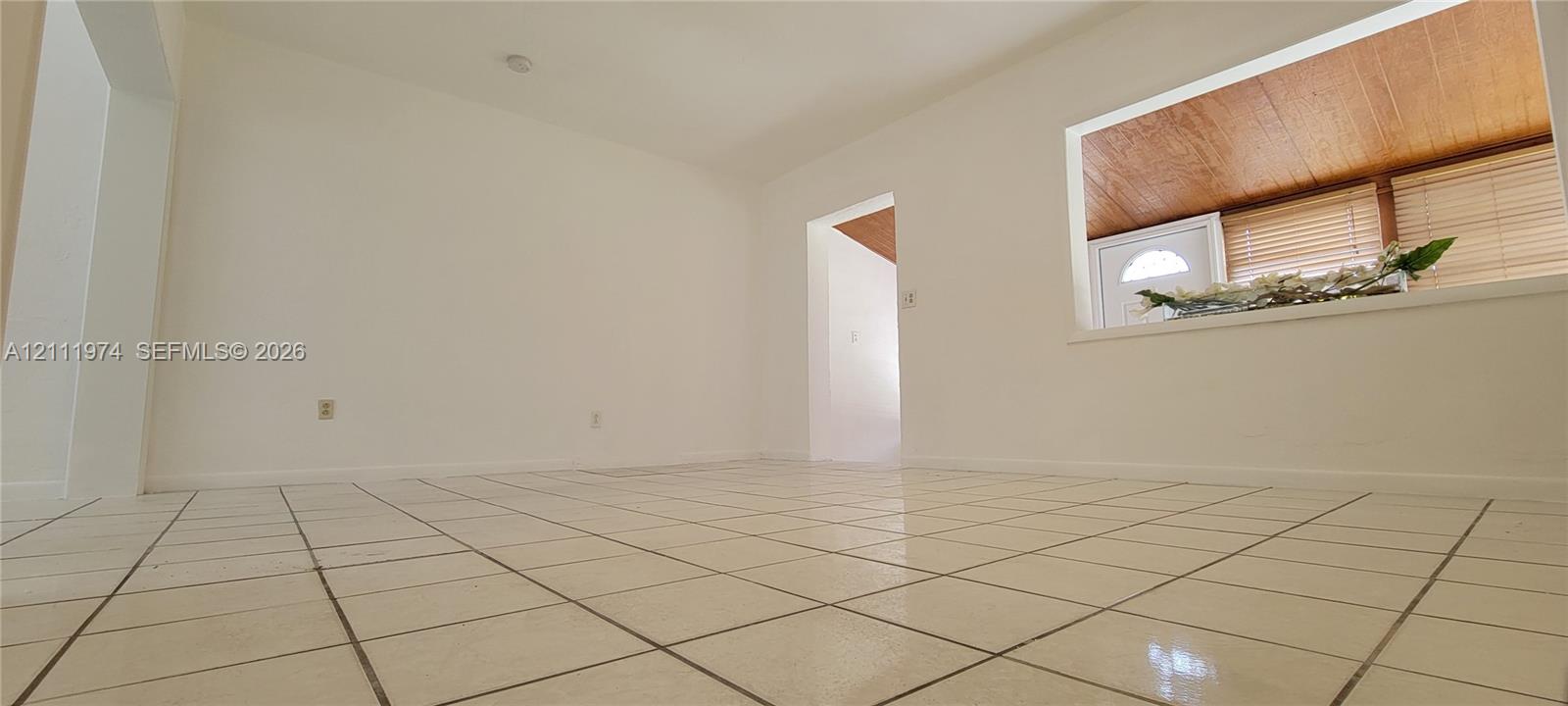 Interior space featuring white walls, square ceramic tile flooring, and a large pass-through opening