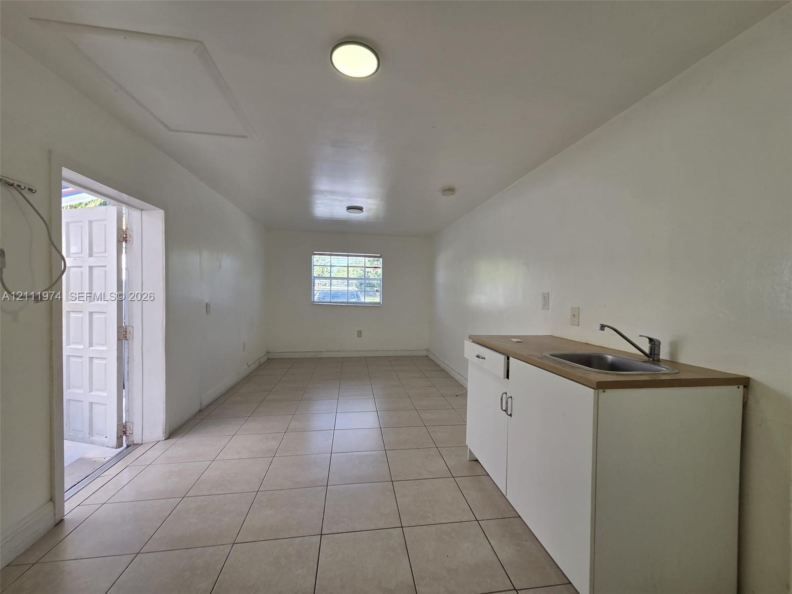 Interior space featuring neutral ceramic tile flooring, built-in cabinetry with a countertop, stainless steel sink with a goose-neck faucet, and exterior access via a multi-panel door