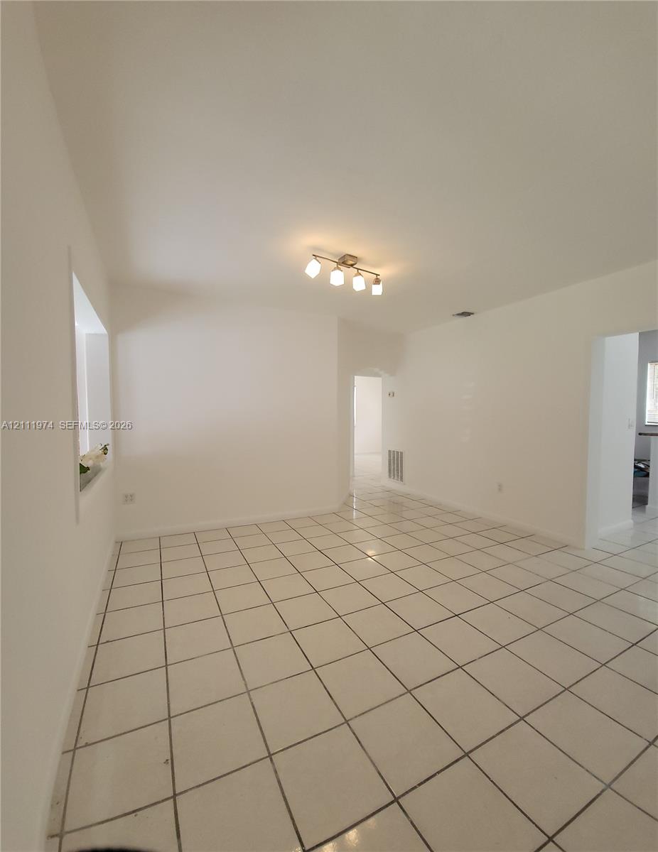 Neutral-toned interior featuring square ceramic floor tiling, smooth walls, and a four-light ceiling-mounted fixture