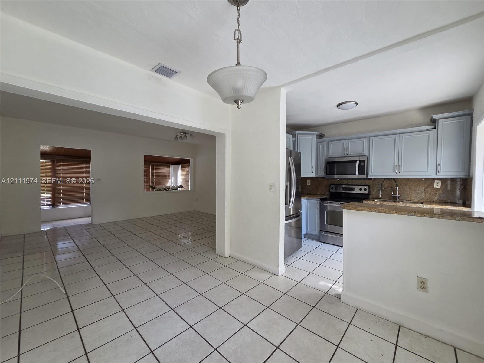 Kitchen featuring shaker-style cabinetry, stone countertops, stainless steel appliances, ceramic tile flooring, and a pendant light fixture