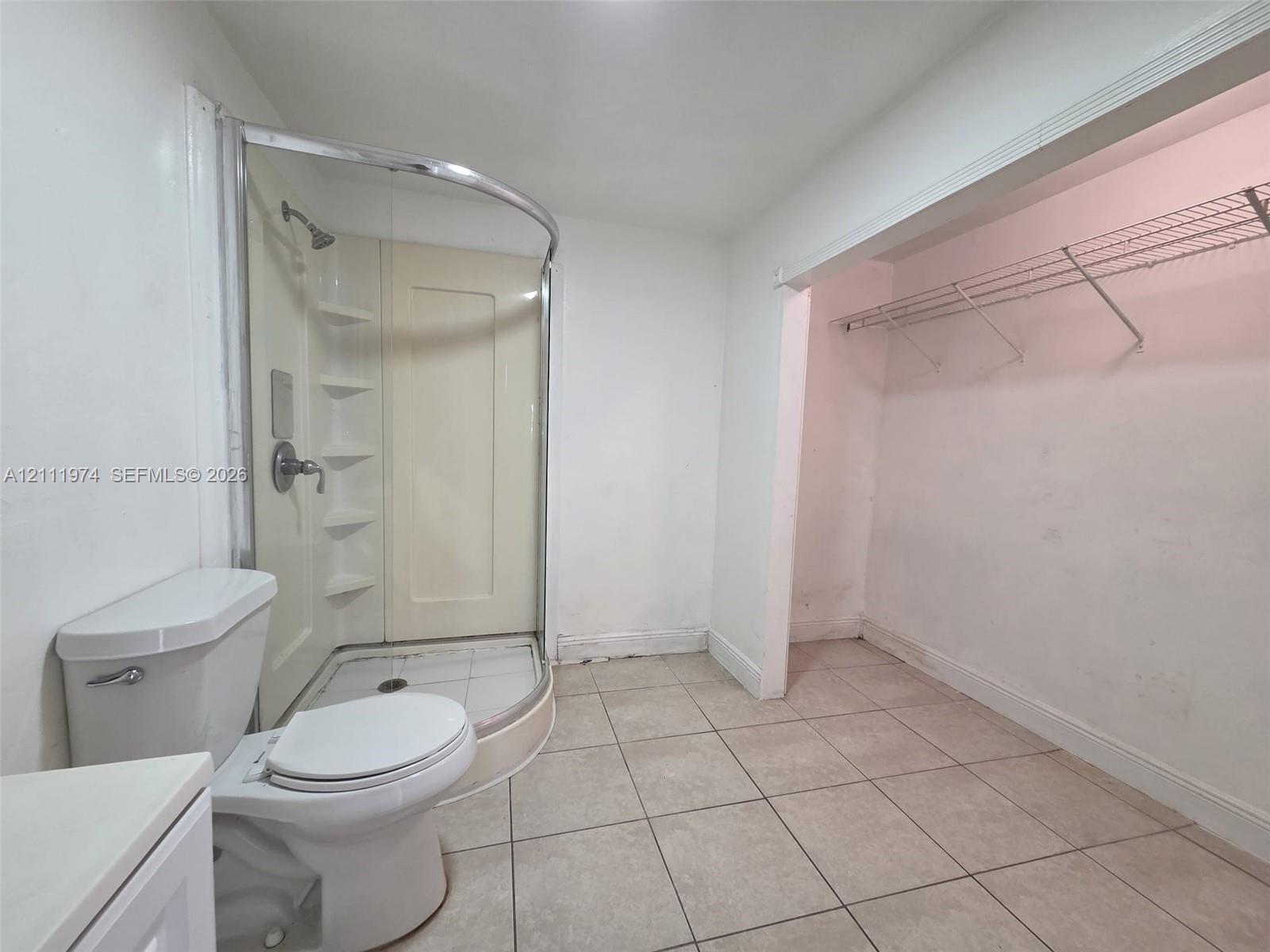 Curved glass shower enclosure with integrated shelving, tile flooring, and built-in wire closet shelving