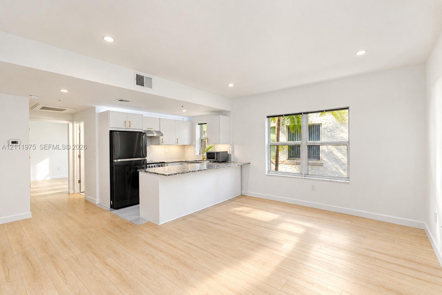 Living roomcountertops, white cabinetry, integrated black refrigerator, wood-finish flooring, and recessed lighting