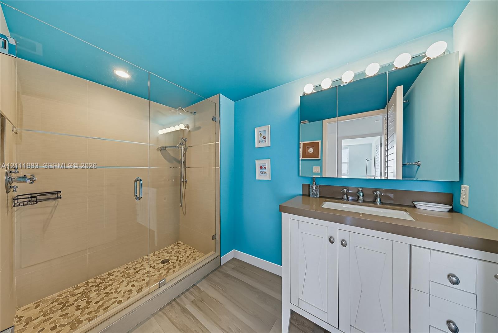 Walk-in shower with a glass enclosure, pebble-tile flooring, and built-in shelving, complemented by a white vanity with an integrated sink, stone-finish countertop, and a mirrored medicine cabinet