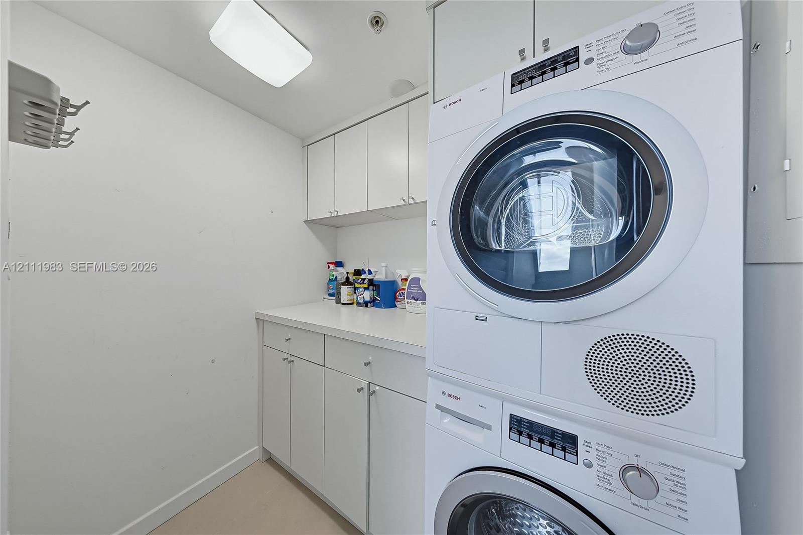 Laundry space featuring stacked front-load washer and dryer, solid-surface countertop, and extensive built-in white cabinetry