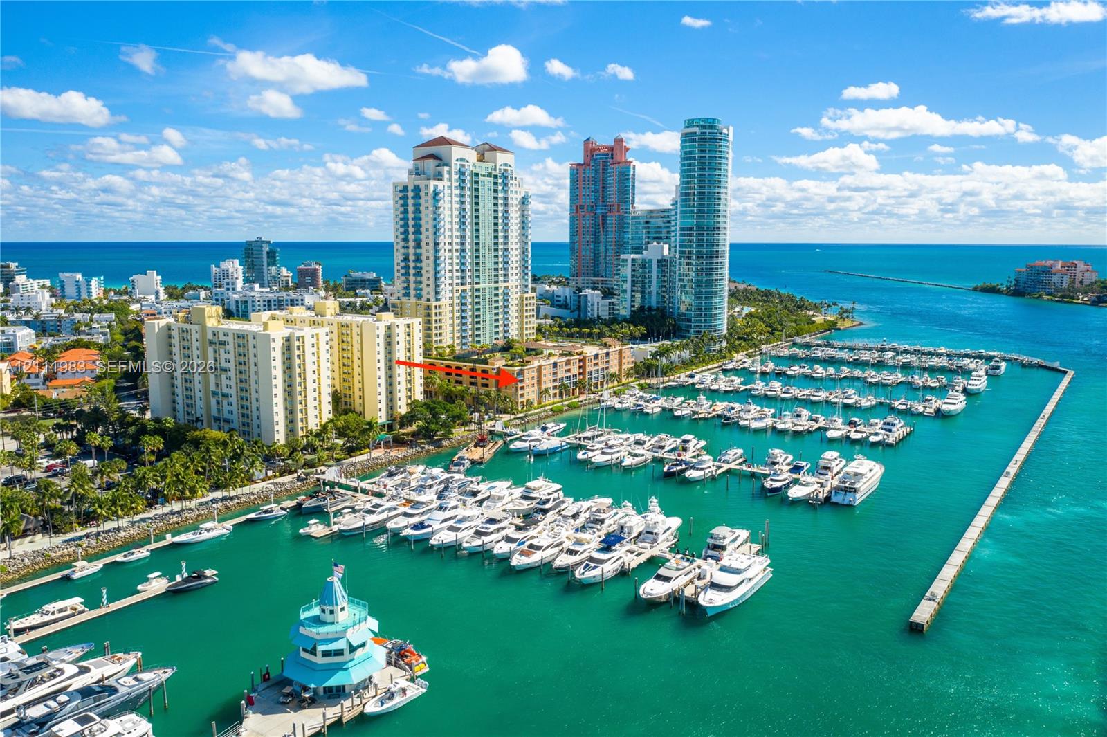 Aerial perspective of a high-rise residential building situated on a waterfront marina featuring multiple boat slips and docking facilities