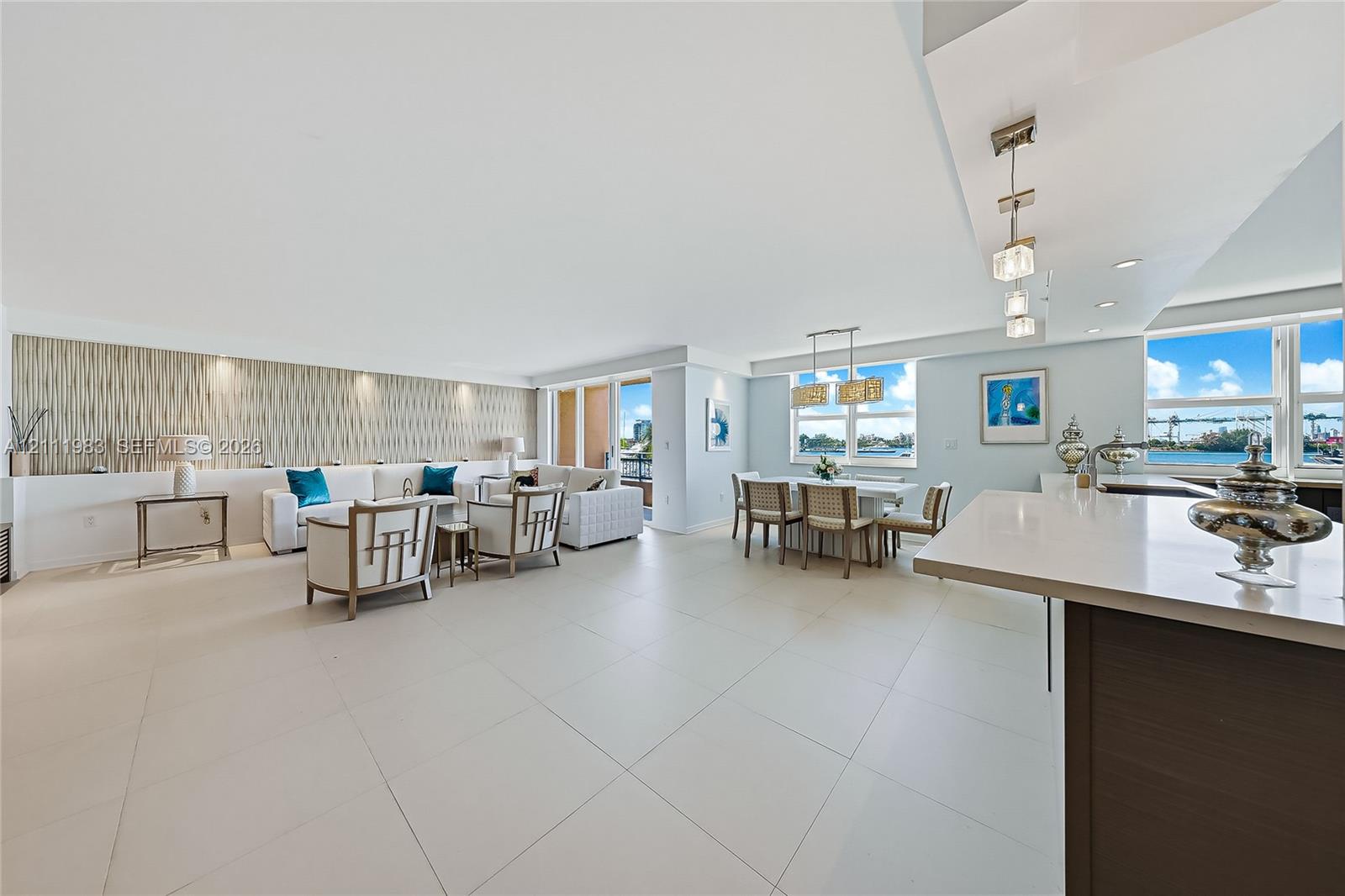 Open-concept interior featuring large-format tile flooring, a stone-surfaced island, textured feature wall with recessed lighting, and expansive windows