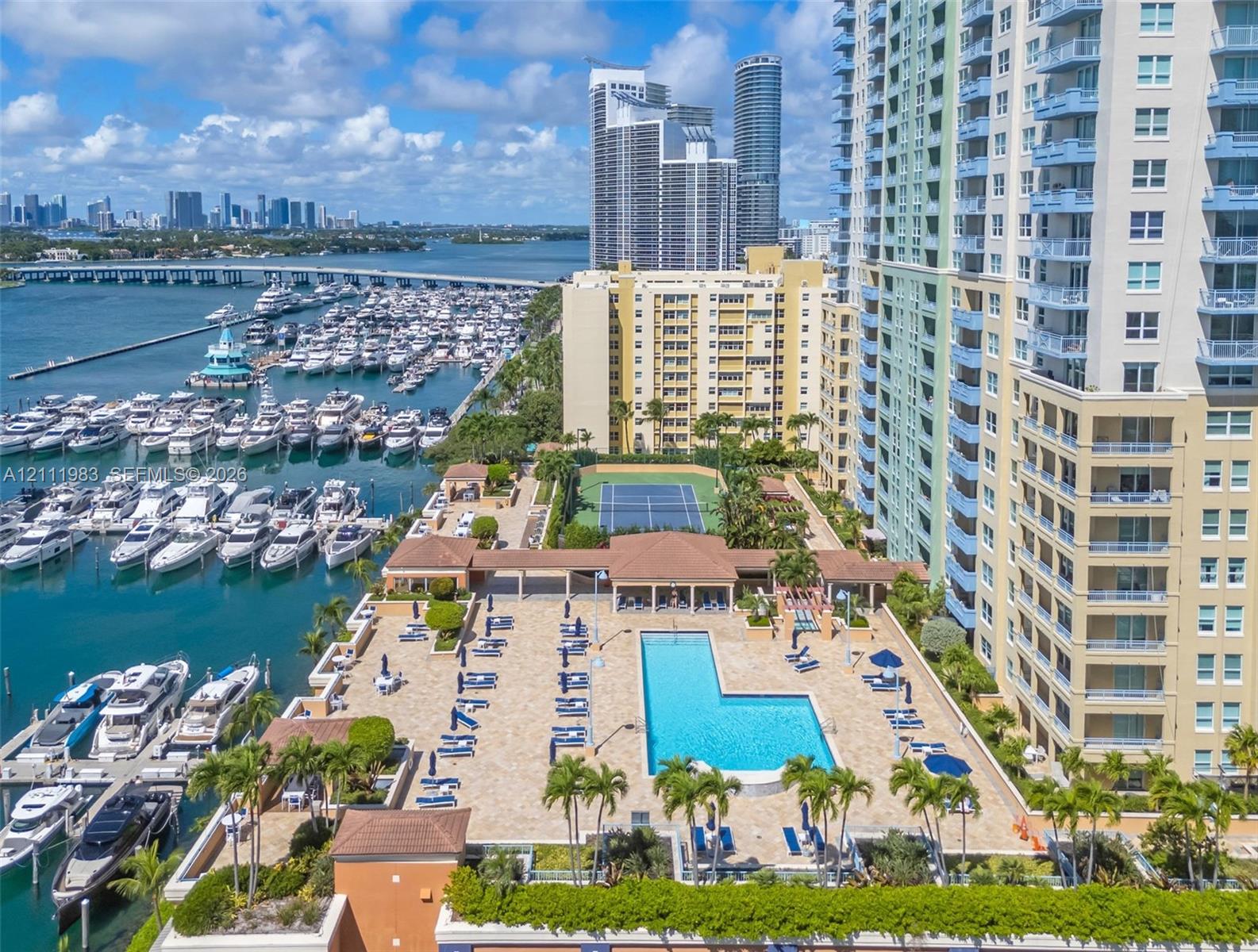 Outdoor recreational area featuring a paved pool deck, swimming pool, and tennis court, situated directly on a deep-water marina