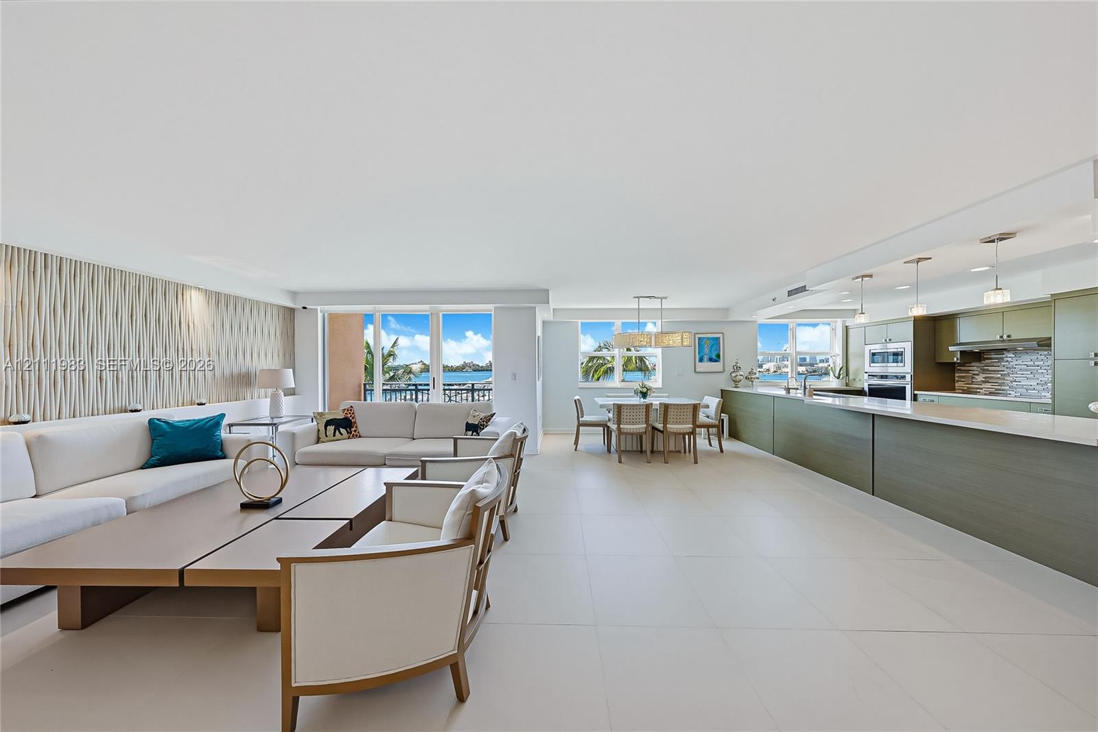 Open-concept living space featuring large-format tile flooring, textured accent wall, integrated kitchen cabinetry, stainless steel built-in appliances, and expansive glass sliding doors
