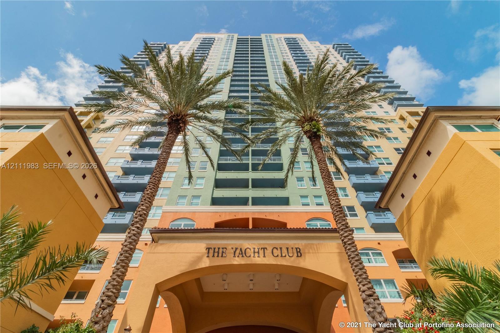 High-rise residential exterior featuring multi-story architectural design, private recessed balconies, arched entryway, and mature palm landscaping