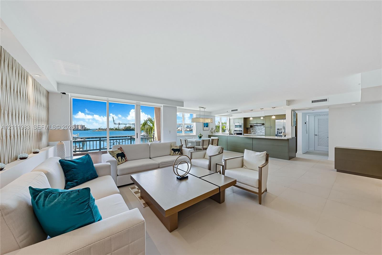Open-concept living area featuring large-format tile flooring, floor-to-ceiling glass sliding doors, textured accent wall paneling, and an island kitchen with quartz countertops Open-concept living area featuring large-format tile flooring, floor-to-ceiling glass sliding doors, textured accent wall paneling, and an island kitchen with quartz countertops