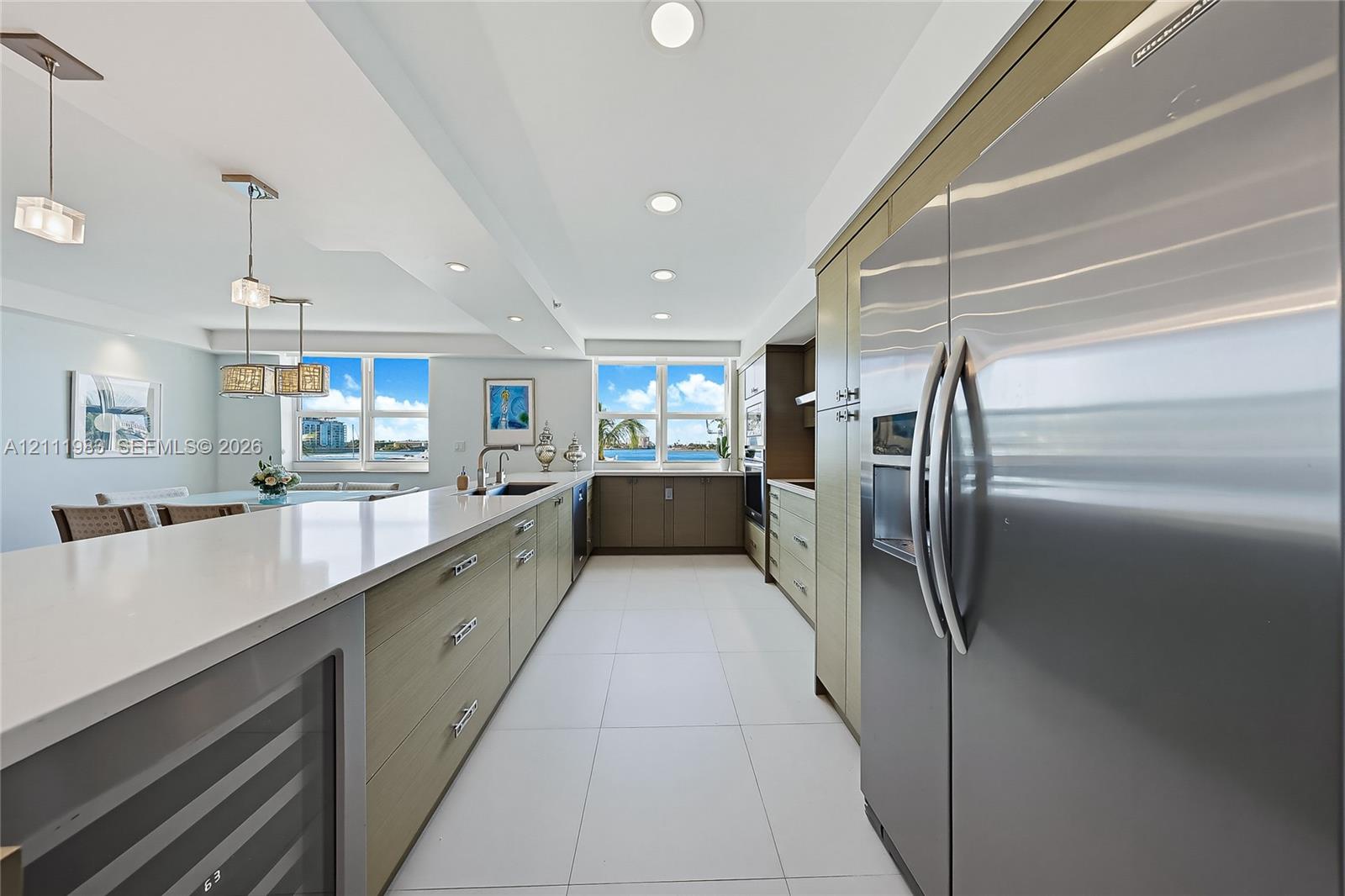Kitchen featuring stainless steel appliances, flat-panel cabinetry, a long island with a solid-surface countertop, tile flooring, and integrated wine refrigeration