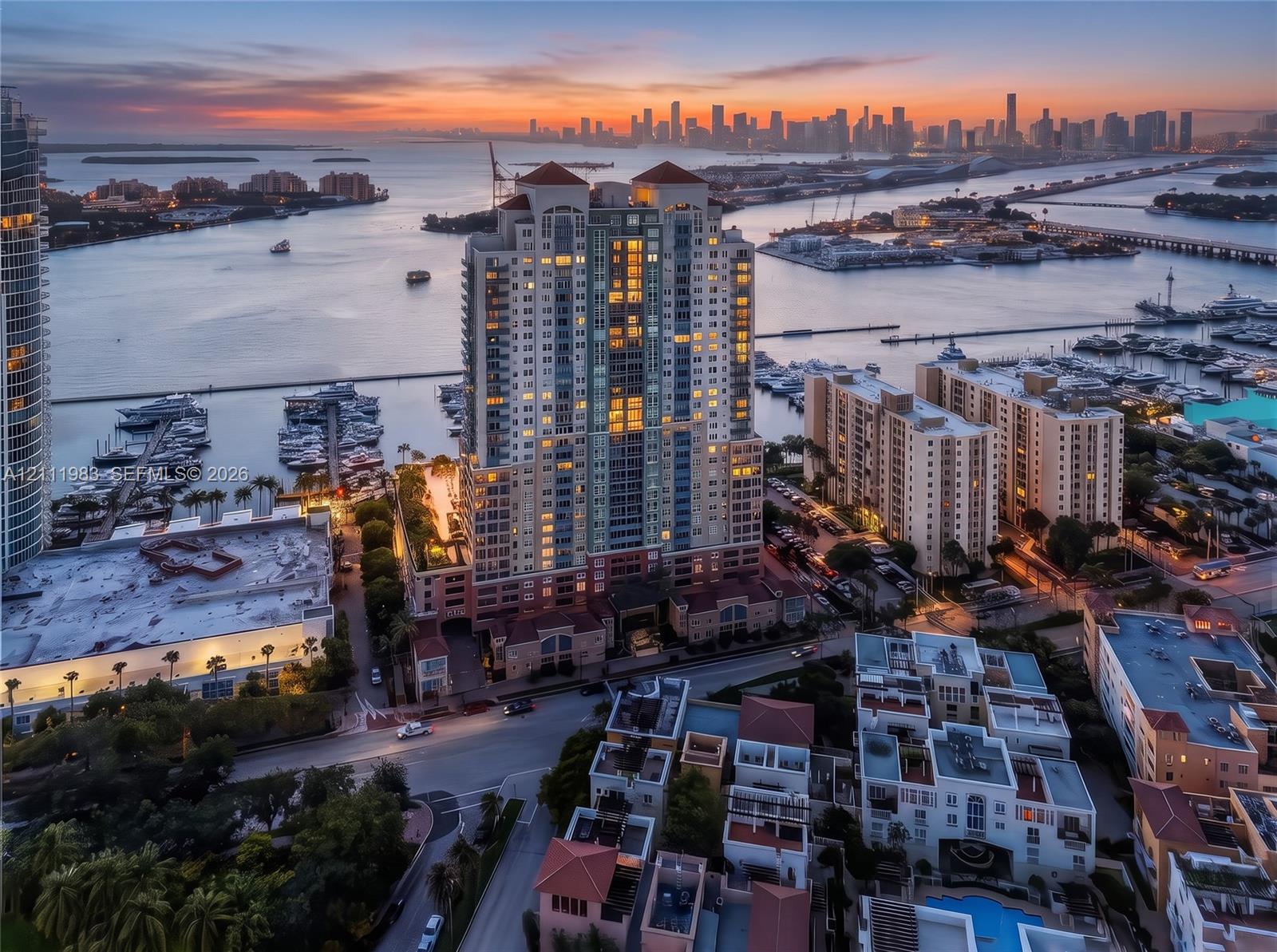 Aerial perspective of a high-rise residential tower featuring a multi-story masonry facade, terracotta-tiled roof accents, private balcony tiers, and a waterfront location