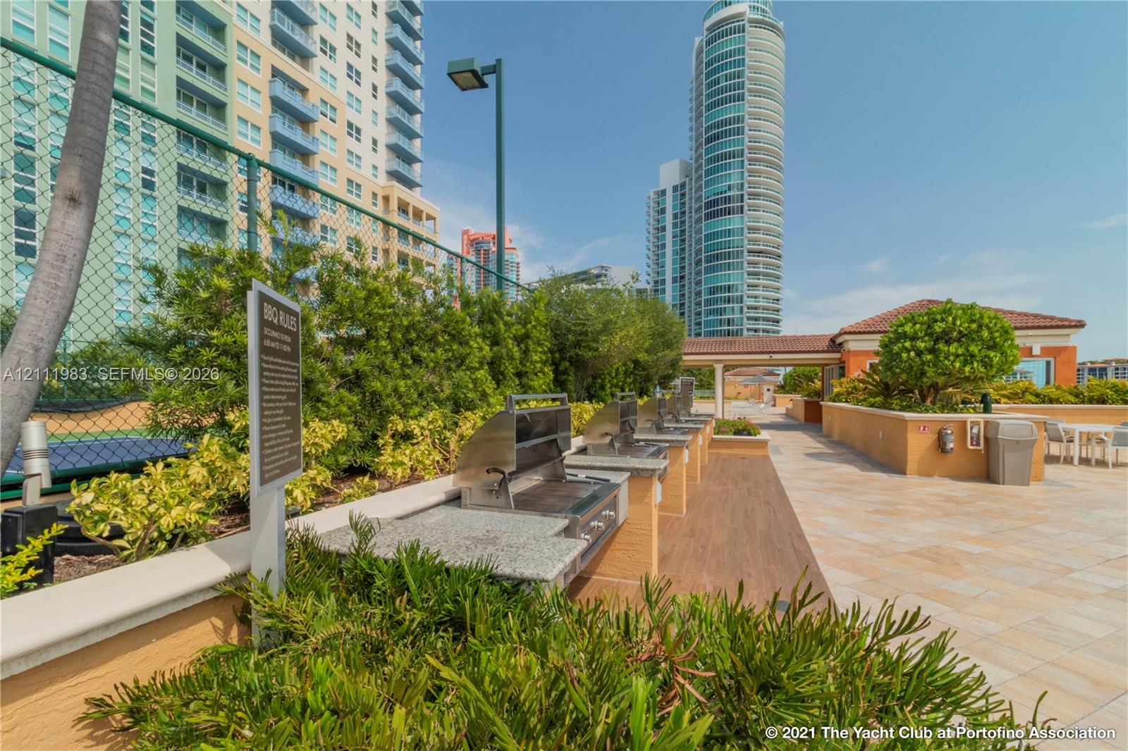 Outdoor grilling area featuring stainless steel built-in barbecue grills, stone-finish countertops, tile flooring, and mature landscaping