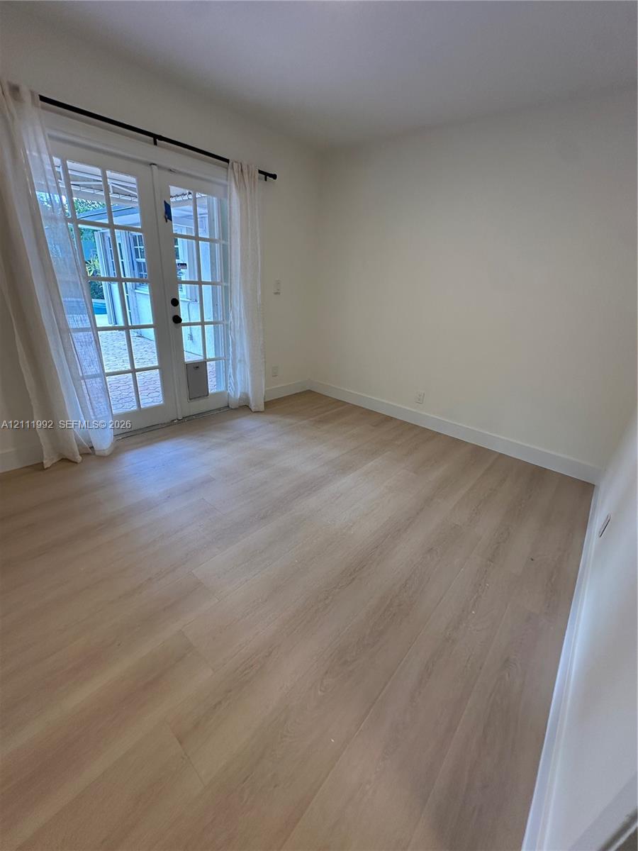 Light-filled room featuring wood-finish flooring, neutral walls, and glass-paned French doors