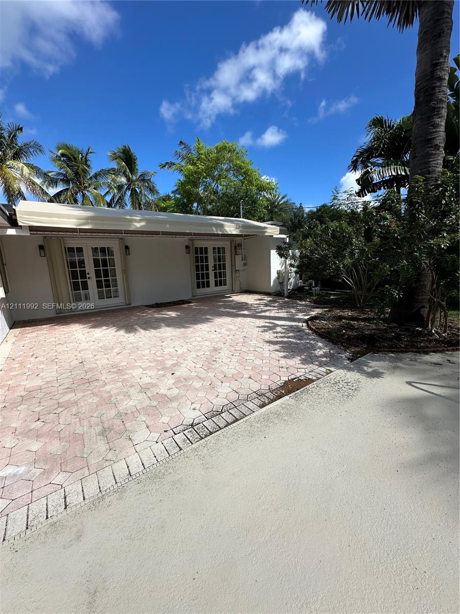 Rear patio featuring decorative concrete pavers, dual sets of French doors, an attached retractable awning, and mature palm landscaping