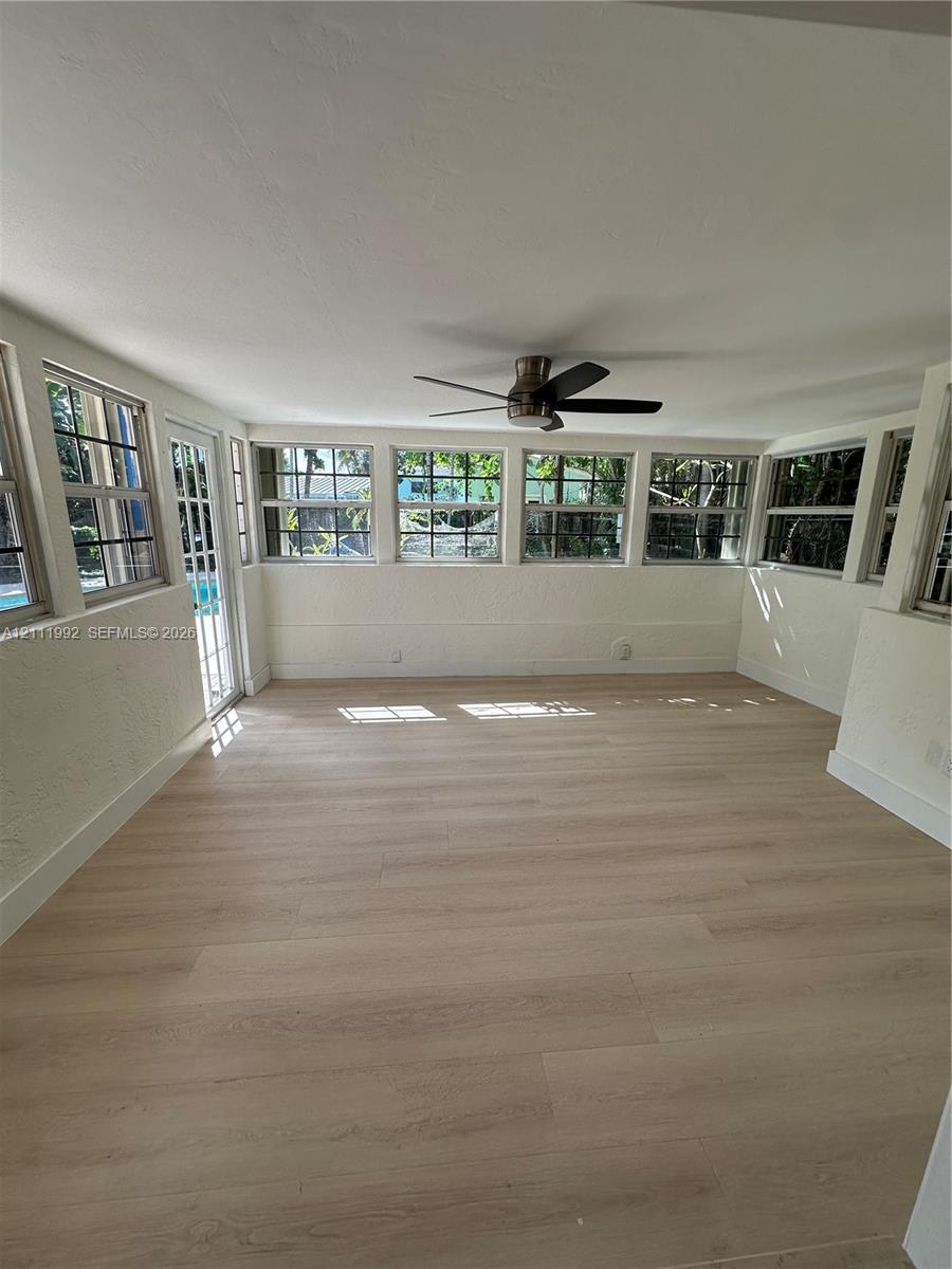 Sunroom featuring wood-finish flooring, a series of multi-pane windows, and an overhead ceiling fan