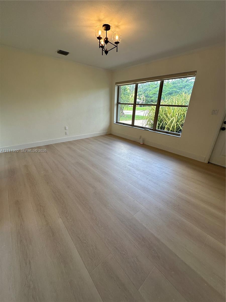 Interior space featuring light-toned wood-finish flooring, a multi-light metal chandelier, and a large window with exterior greenery