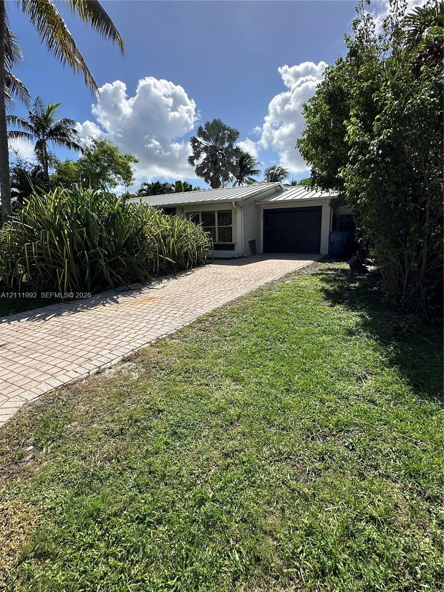 Single-story exterior featuring a metal roof, paver driveway, and attached garage