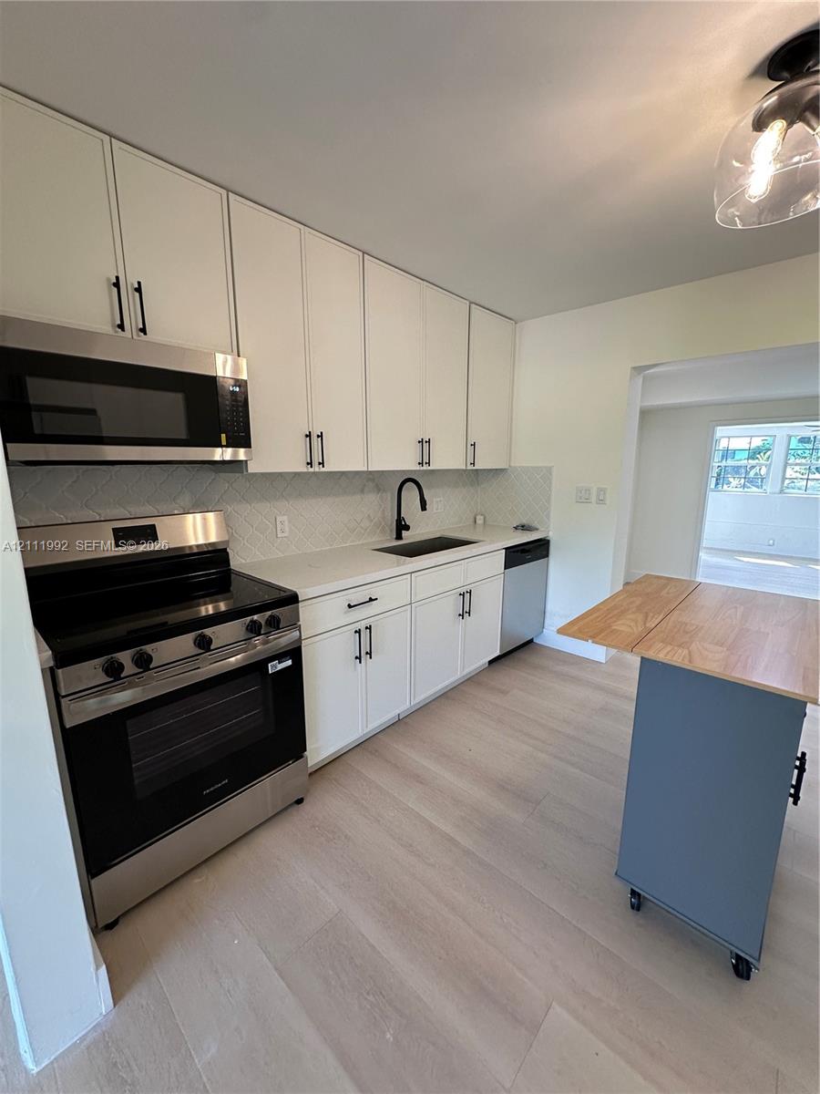 Kitchen featuring white shaker-style cabinetry, stainless steel appliances, white stone-finish countertops, geometric-patterned backsplash, and wood-finish flooring