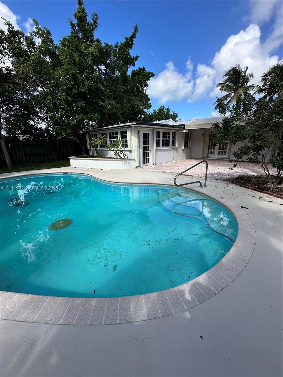 Curved inground pool with metal handrail, paver patio, and low-profile exterior masonry wall
